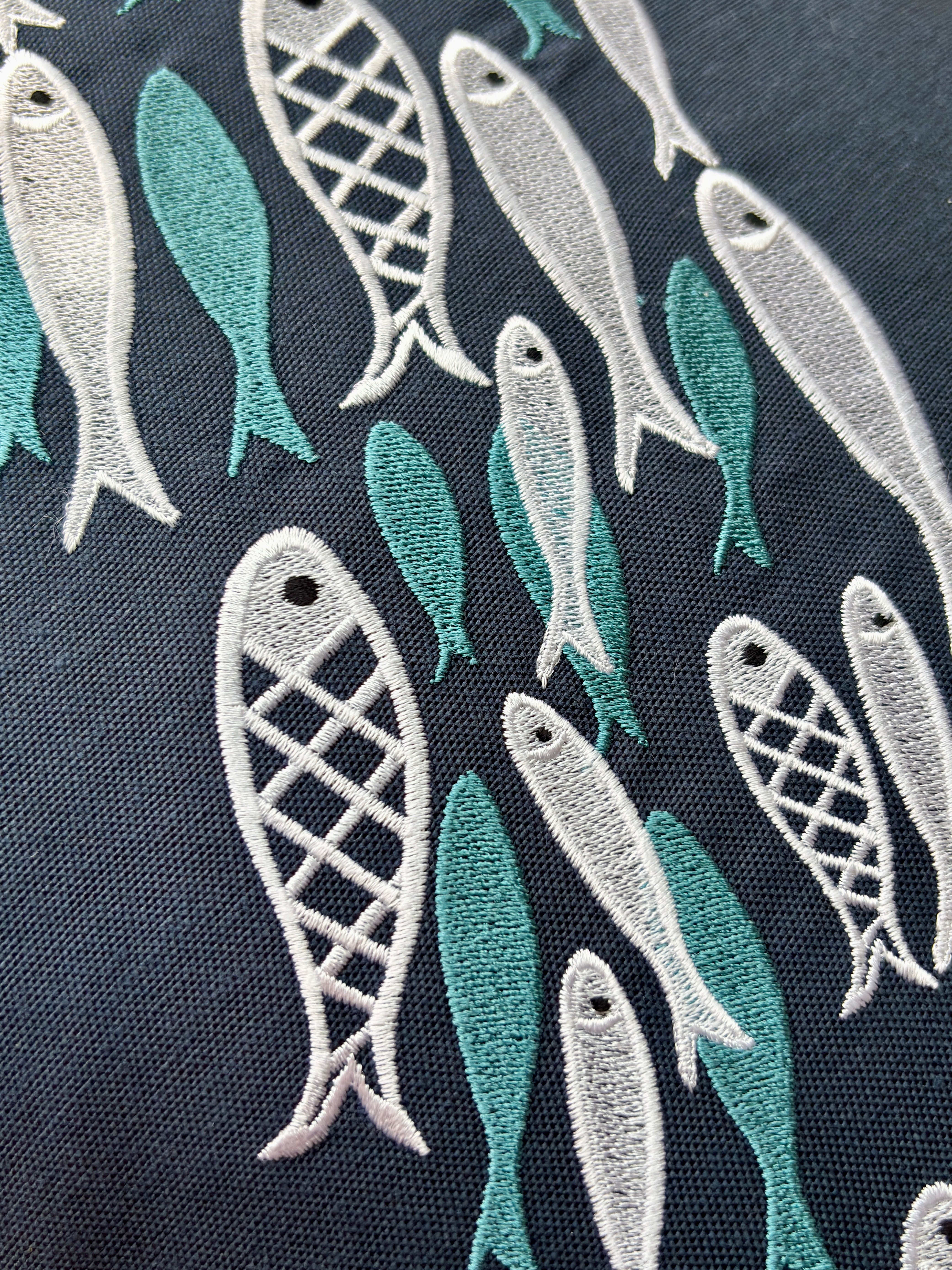 Aqua Dance decorative pillow in azure color, measuring 18 x18 inches, featuring three overlapping teal fish-shaped embroidery designs on a rectangular blue fabric. Designed for life at sea, it combines durability, elegance, and a tranquil marine-inspired aesthetic.