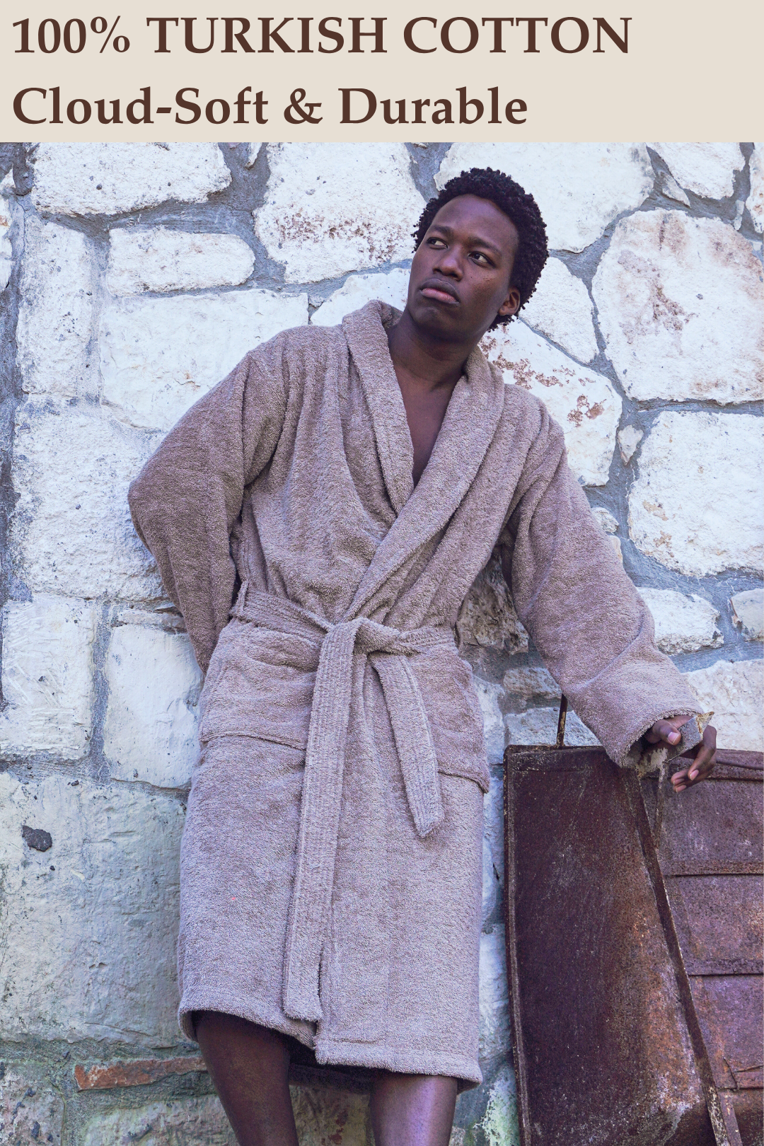 A man leaning against a stone wall outdoors wearing a plush, cloud-soft Harbour Loom 100% Turkish cotton mens bathrobe in taupe brown