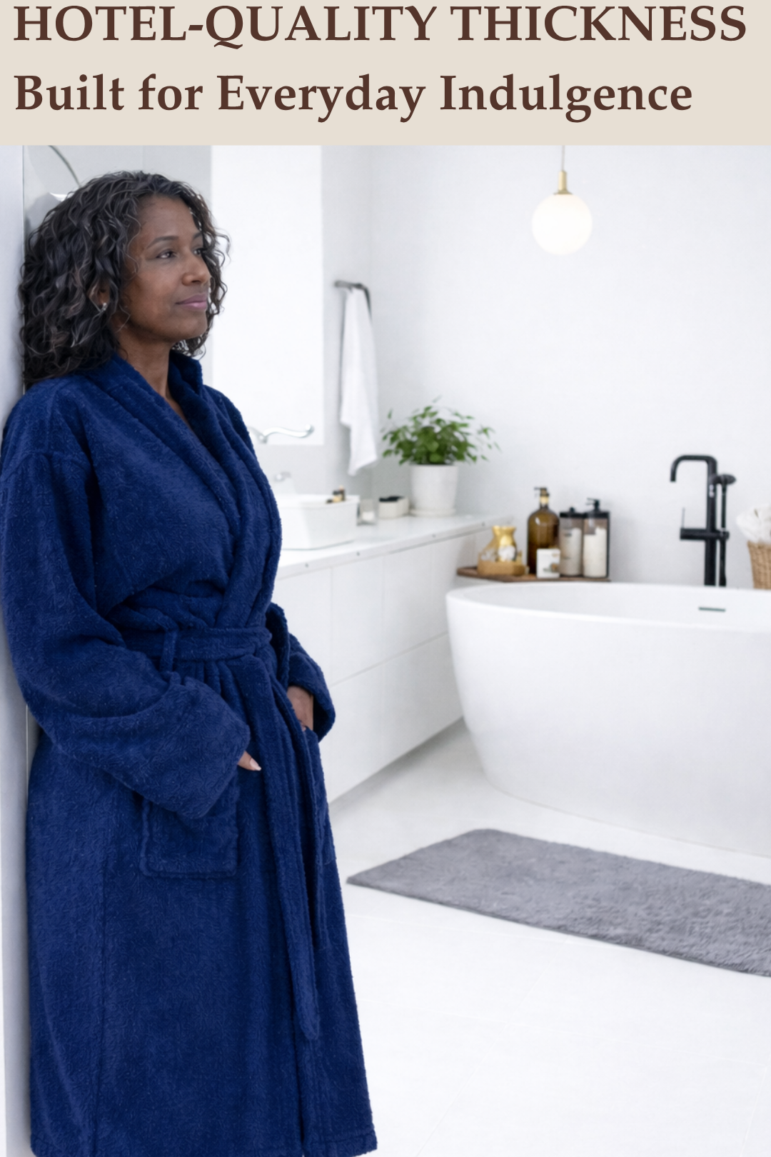 A woman relaxing in a modern white bathroom wearing a thick, hotel-quality navy blue terry cloth bathrobe.