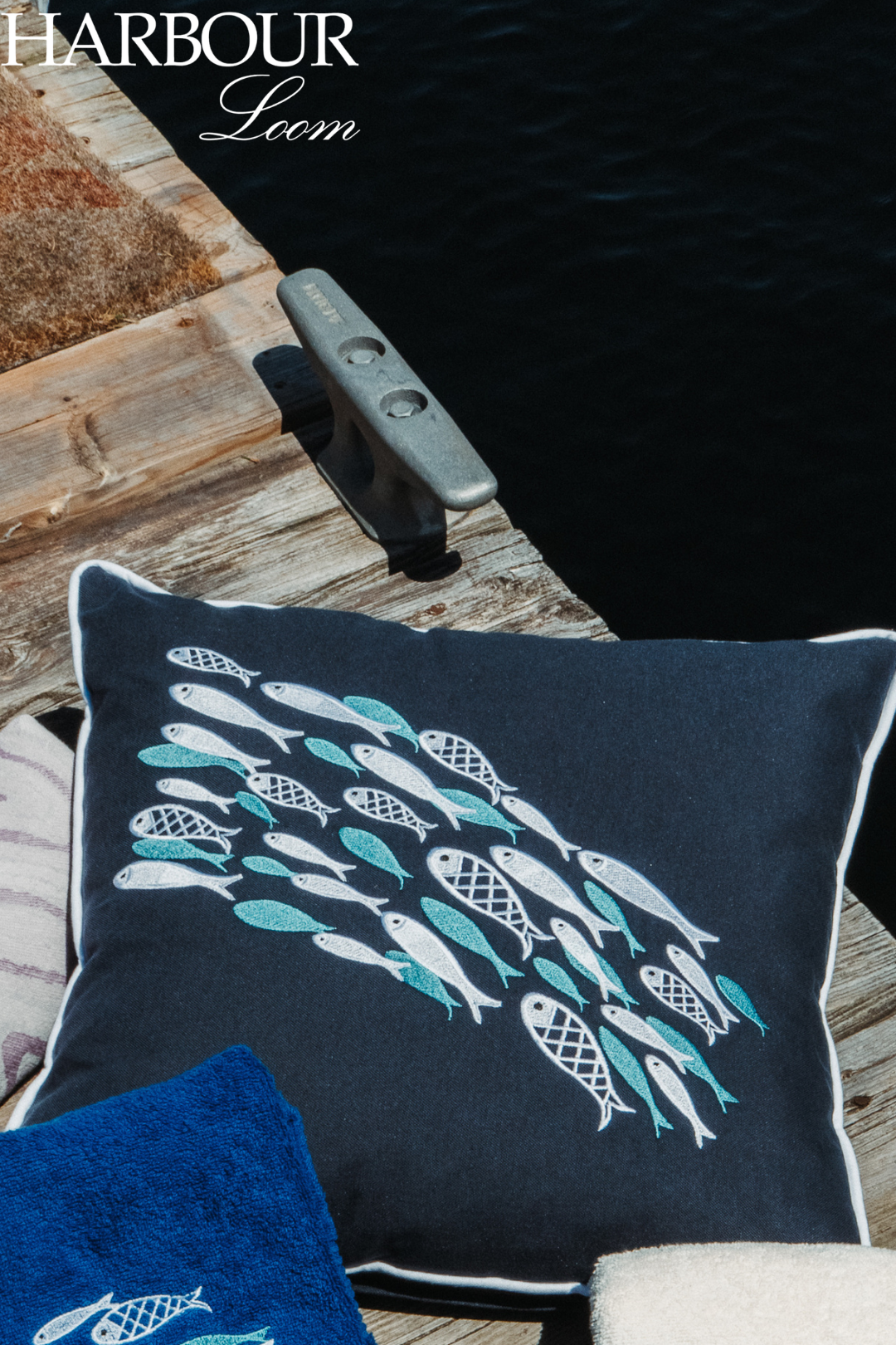 Navy pillow with fish pattern on a wooden surface, branded 'Harbour Leem'.