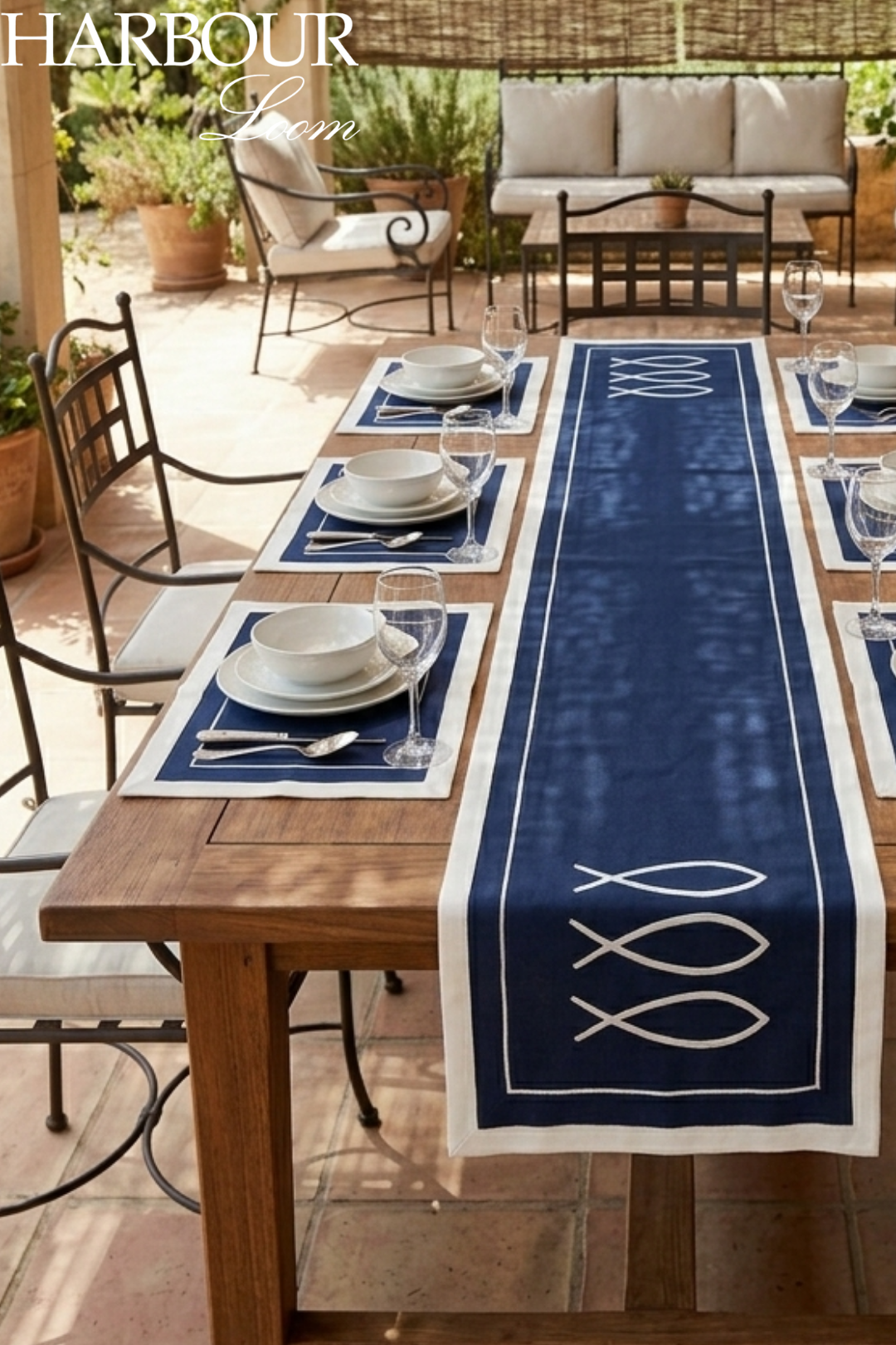 Table setting with a blue table runner featuring white fish designs in an outdoor patio setting.