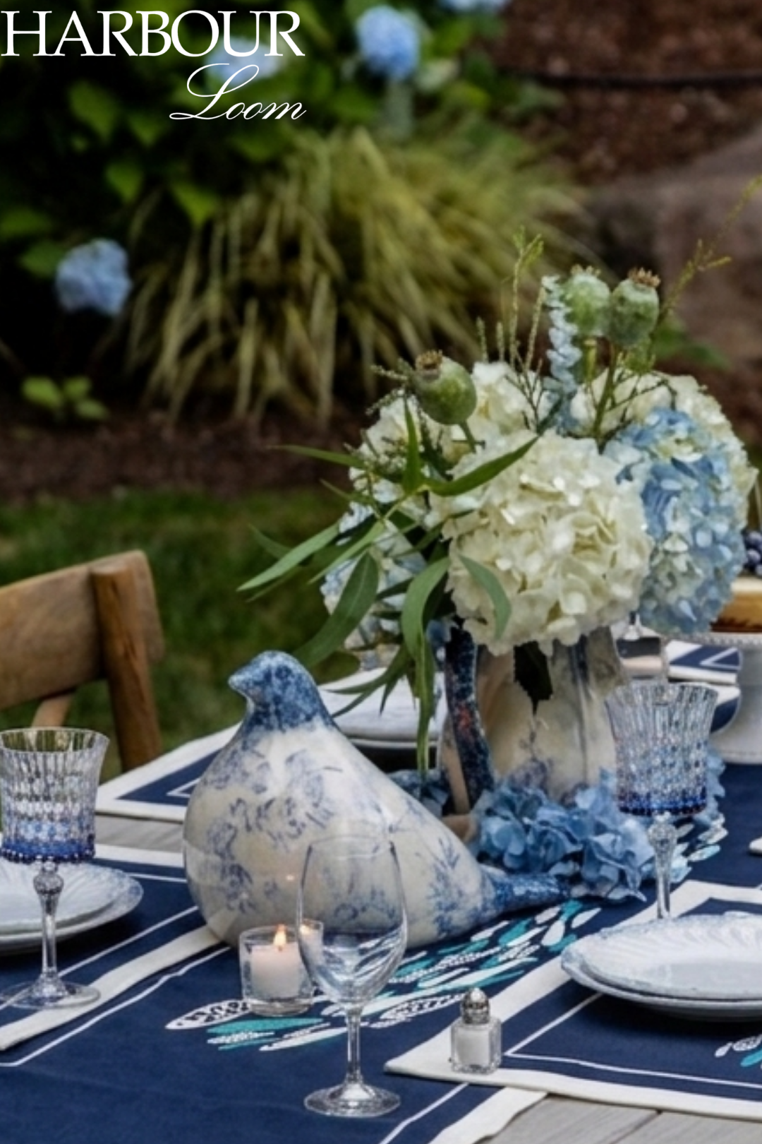 Table setting with blue and white decor, including flowers and tablecloth, outdoors.
